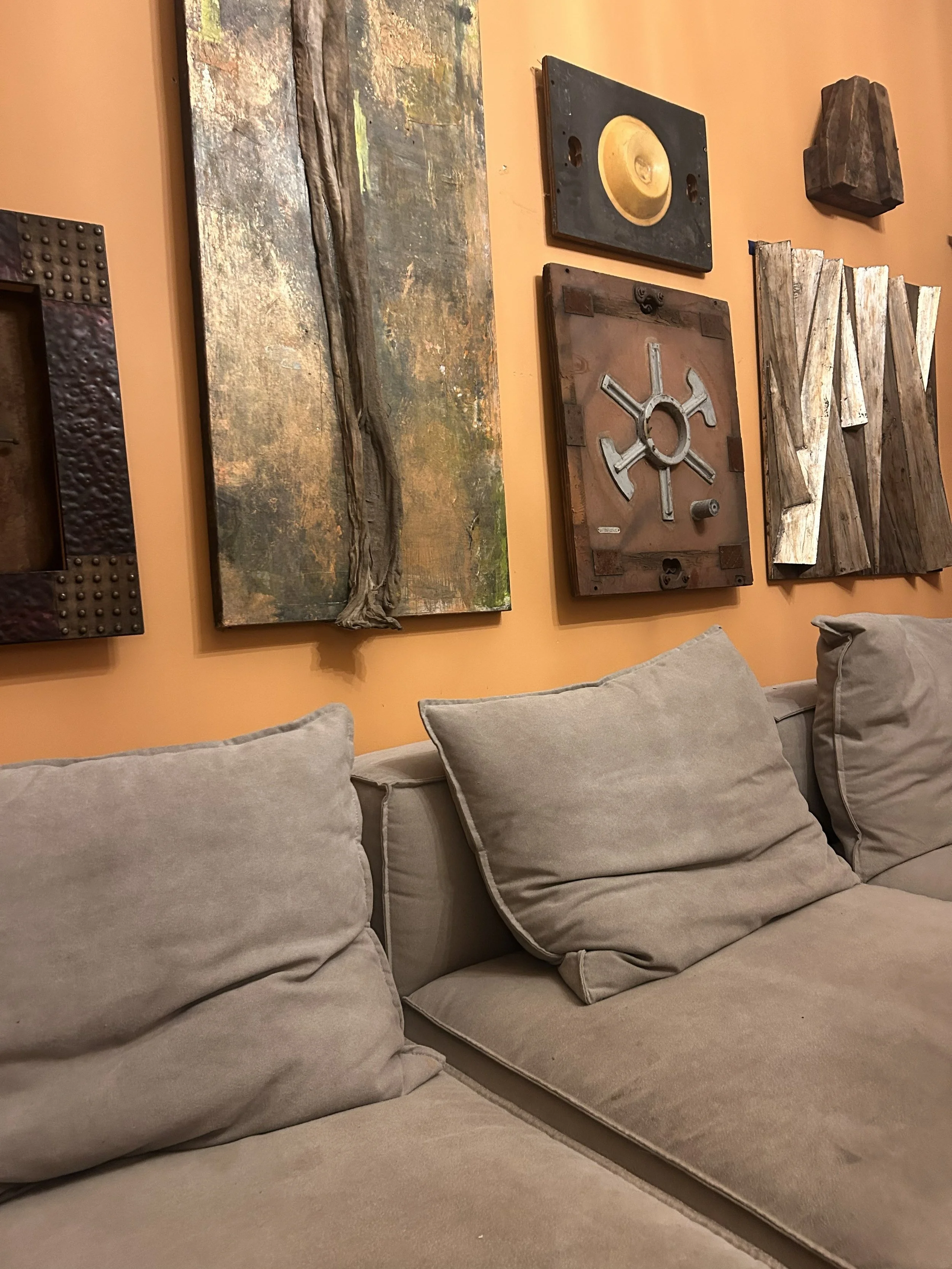 A beige fabric sofa with multiple plush cushions in front of a peach wall decorated with framed rustic artwork.