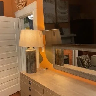 A bedroom with a wooden dresser, a large mirror, a lamp with a marble base, and an orange accent wall.