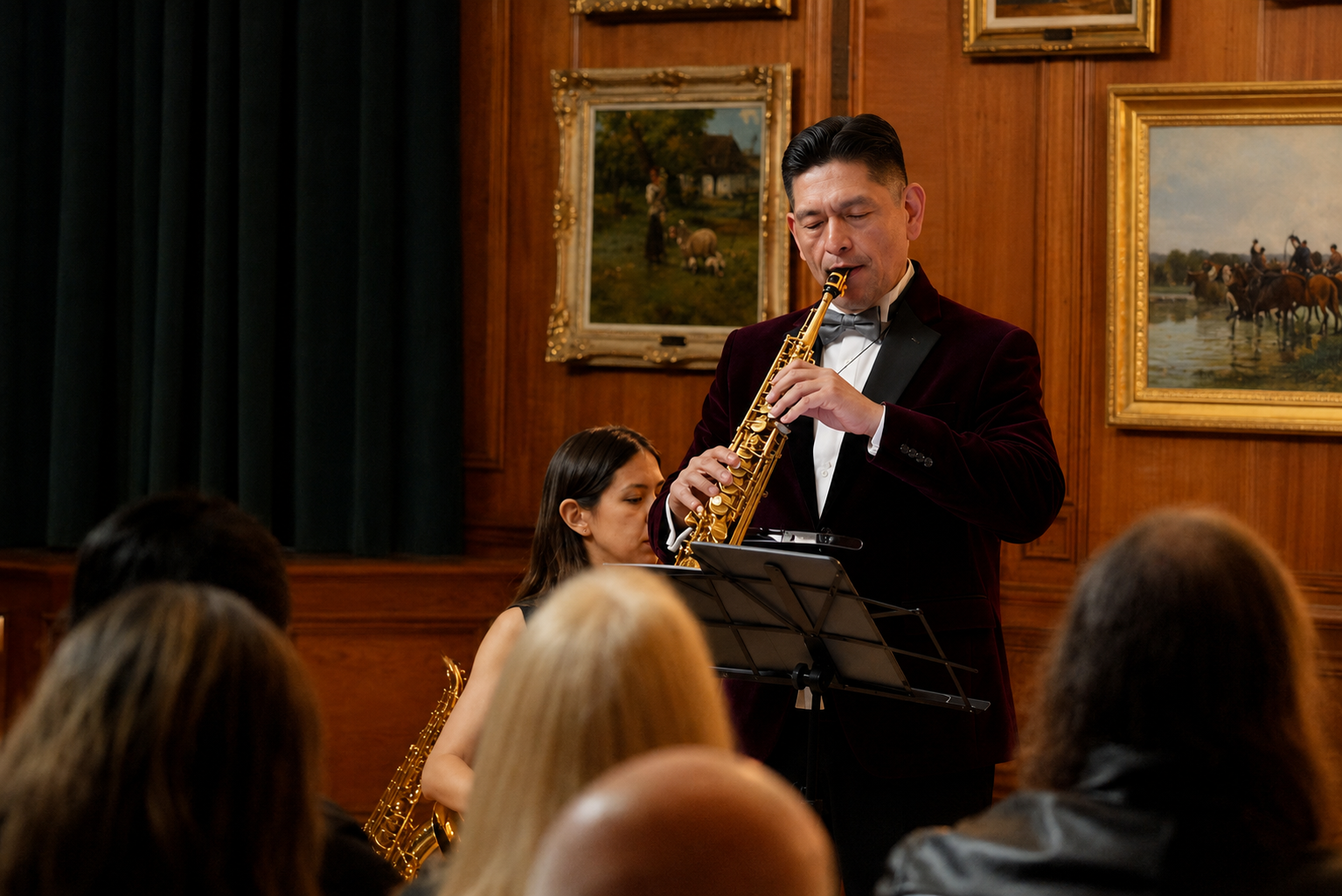 A jazz band performing in an elegant room with framed landscape paintings on wooden walls. A male saxophonist in a dark velvet blazer and bow tie plays to an audience.