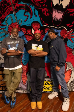 Three men standing in front of a Spider-Man comic book mural. All are smiling and dressed casually.