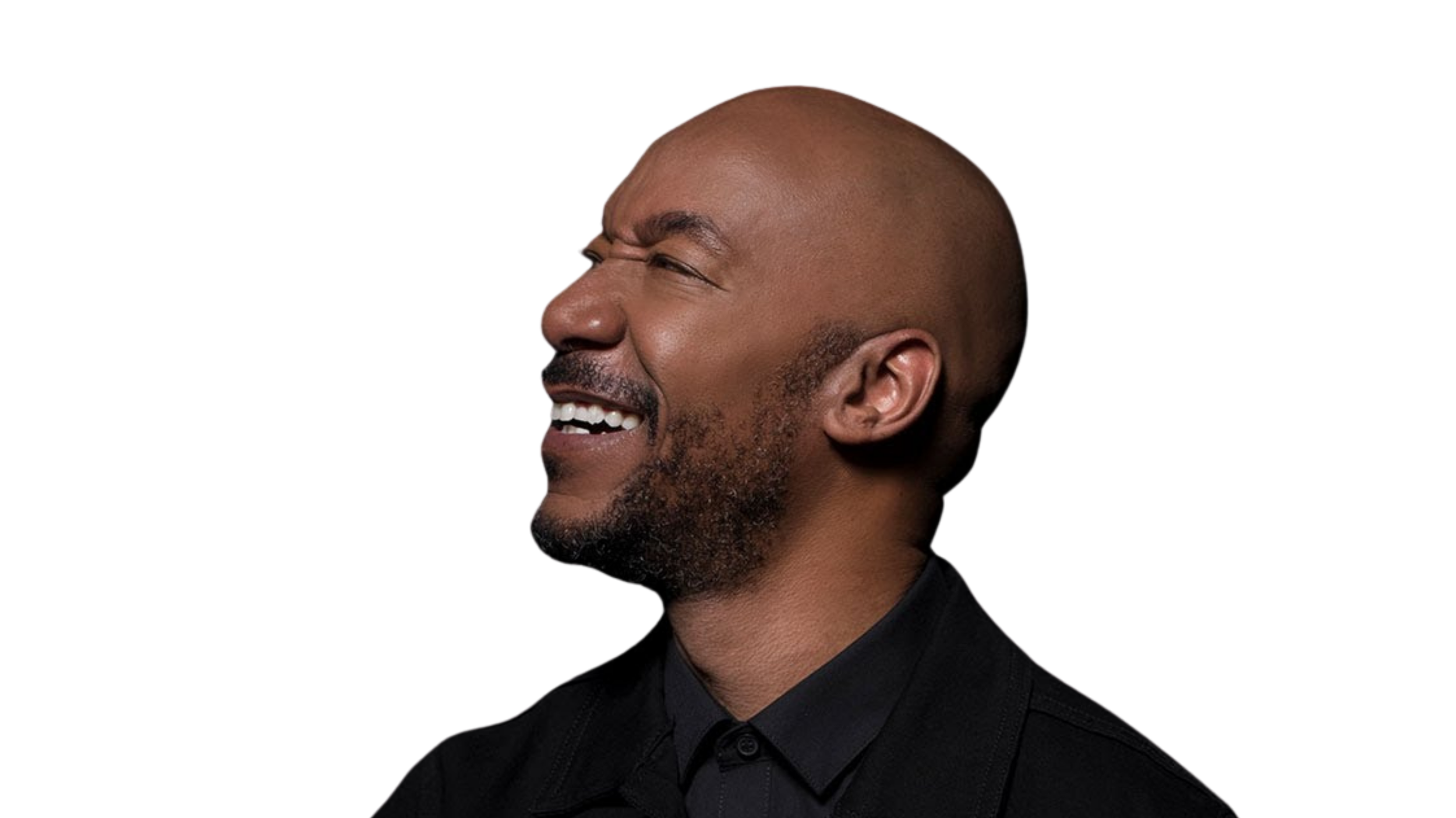 Datwon Thomas, a man with a bald head and beard, wearing a black shirt, laughing with his eyes closed against a black background.