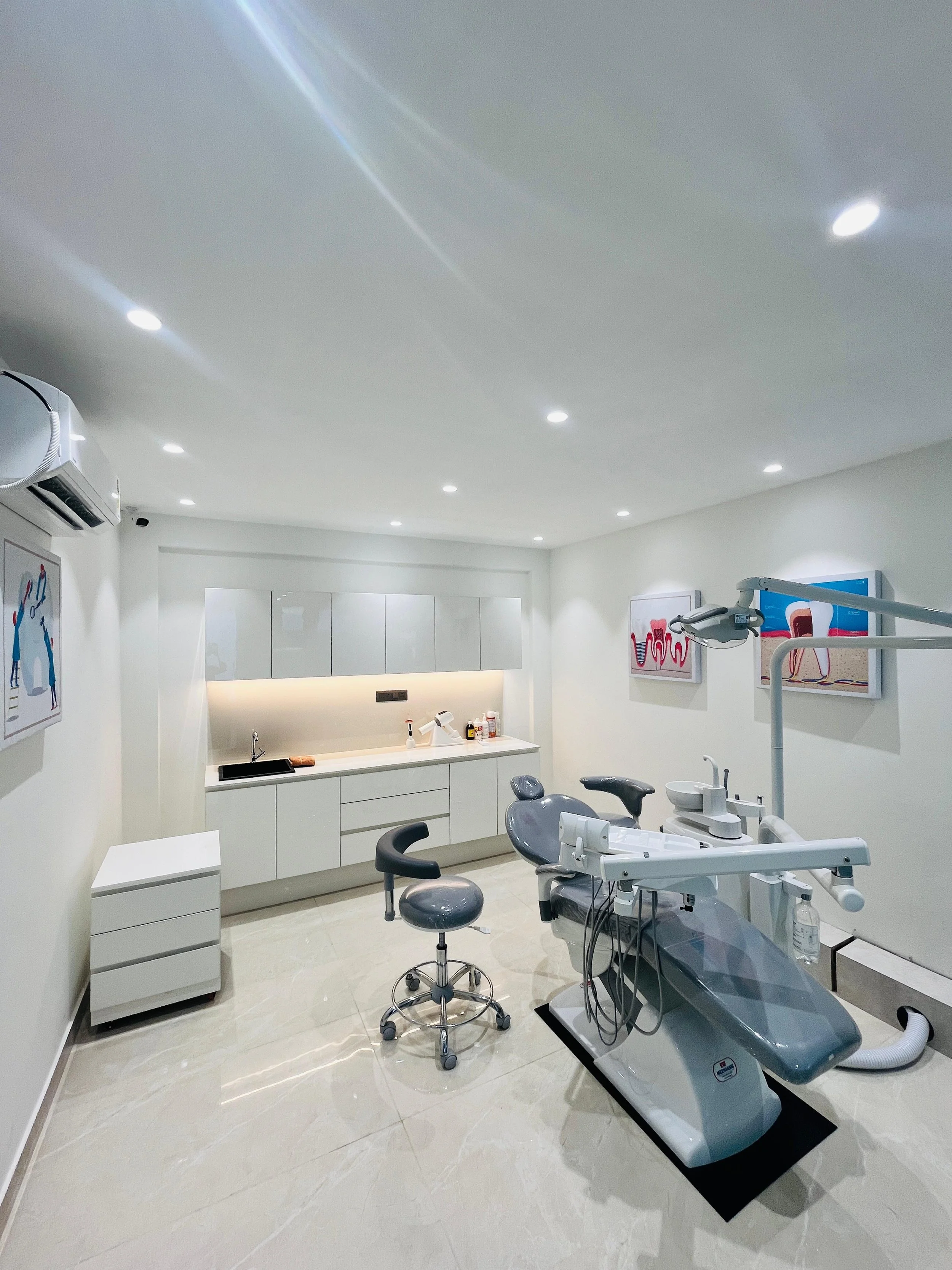 Dental clinic treatment room with dental chair, stool, cabinets, artwork, and equipment.