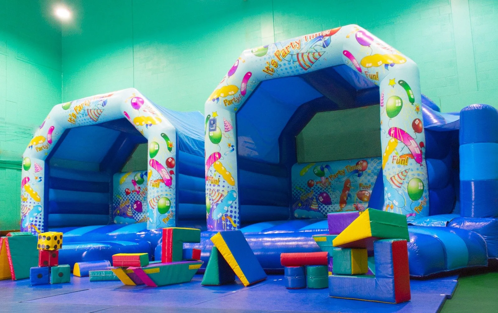 Colorful inflatable bounce house with birthday-themed designs, surrounded by foam blocks on a padded floor