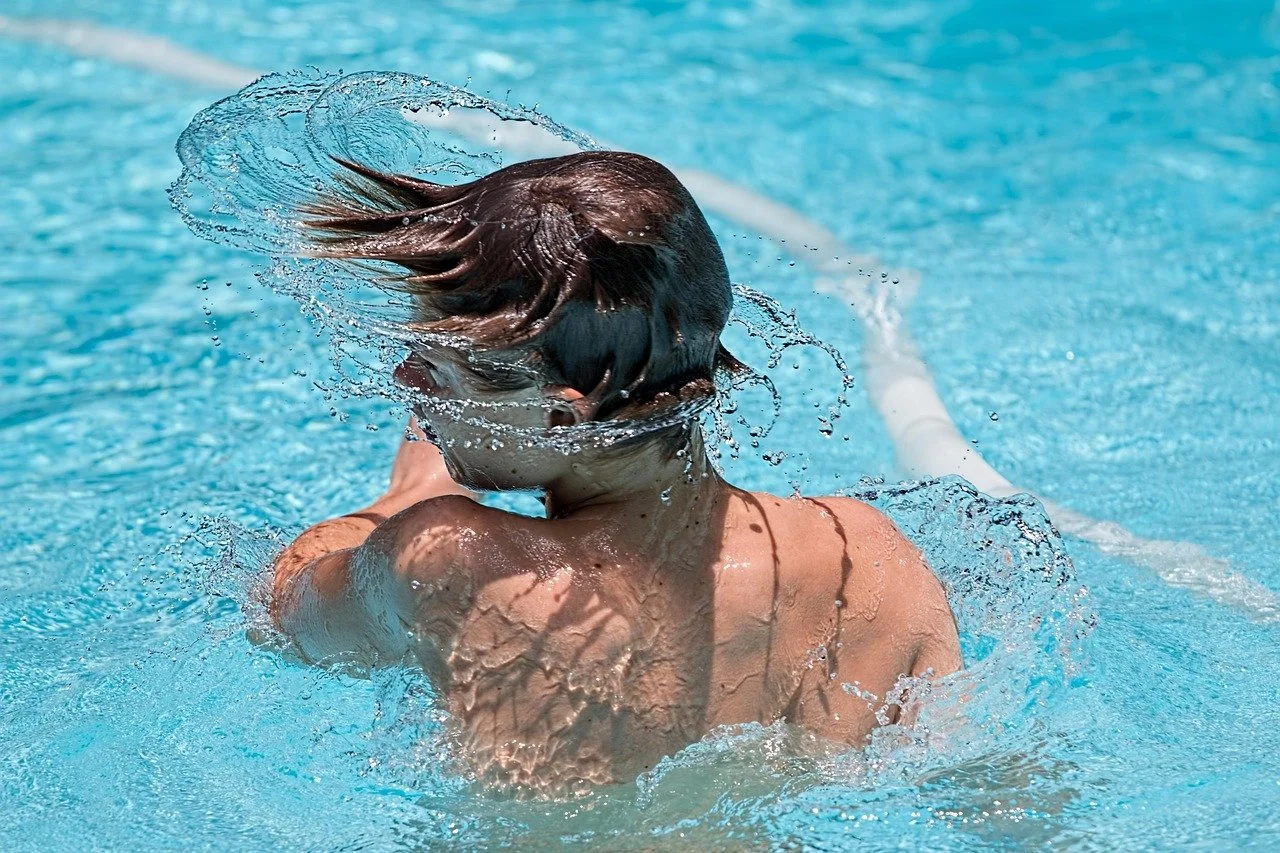 A person swimming in a pool, turning their head underwater with water splashing around.