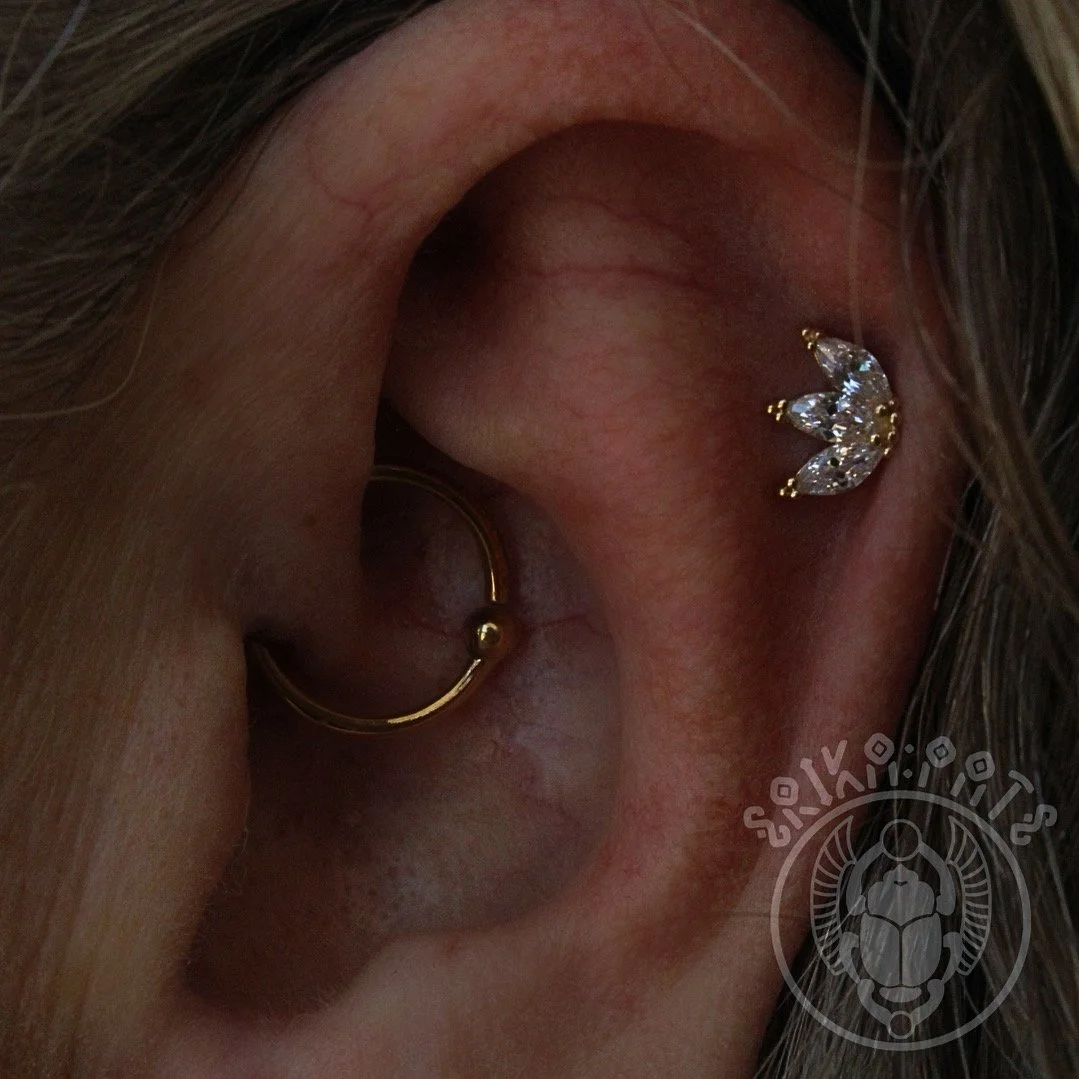 A close-up of a person's ear with two earrings: a gold hoop in the earlobe and a curved gold and diamond cartilage stud in the upper ear.