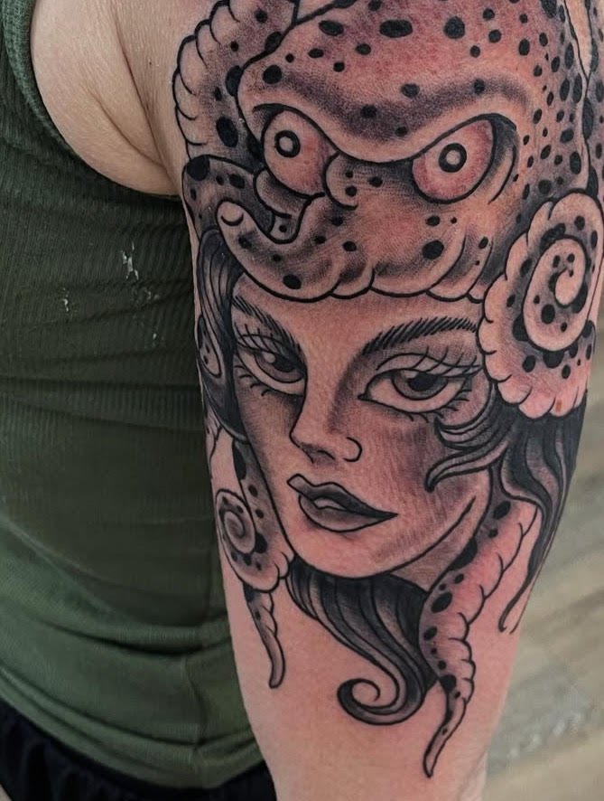 This striking tattoo portrays a woman adorned with an octopus headdress in bold black and grey tones. The fluid tentacles and intense gaze merge beauty with strength in a surreal composition.