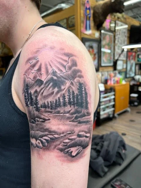 A serene black and grey mountain landscape with trees, clouds, and sunlight breaking through. The soft shading and natural flow capture a peaceful wilderness scene with depth and realism.