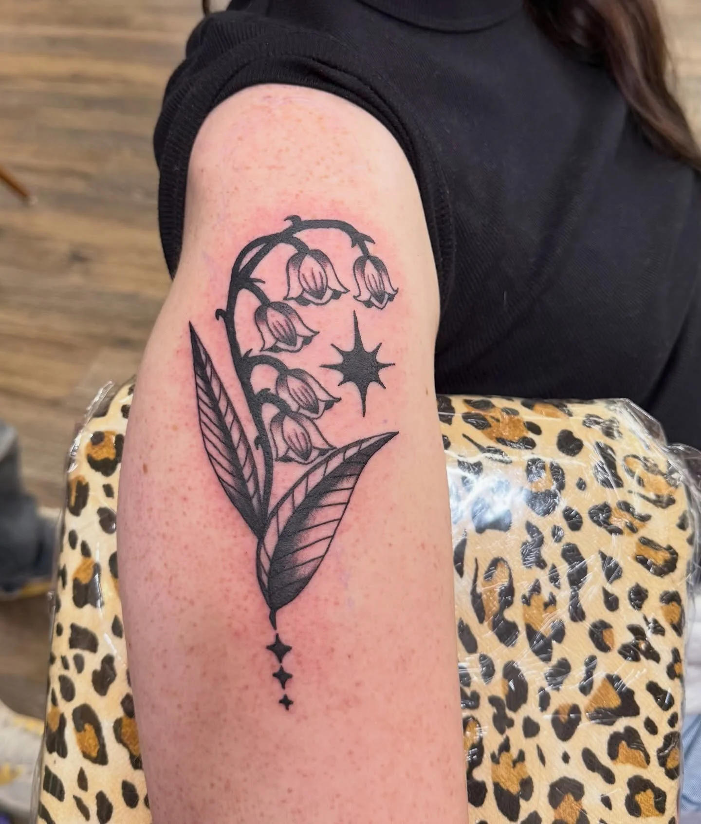 A delicate blackwork tattoo of lily of the valley flowers accented by celestial stars. The clean lines and soft shading highlight the balance between natural beauty and minimalistic elegance.