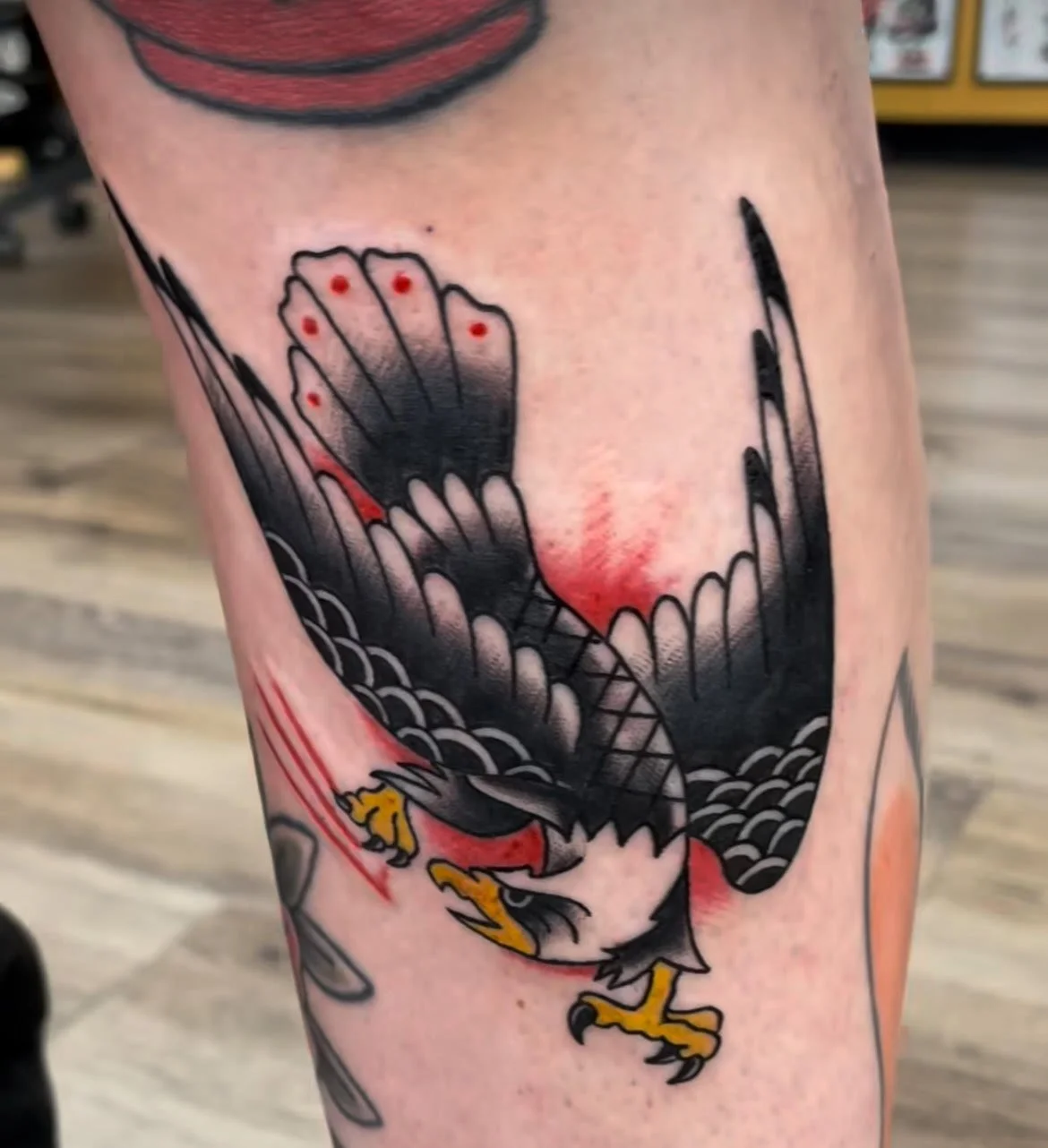 A black and grey eagle mid-dive with red background highlights. The sharp contrast and movement showcase strength and traditional boldness.