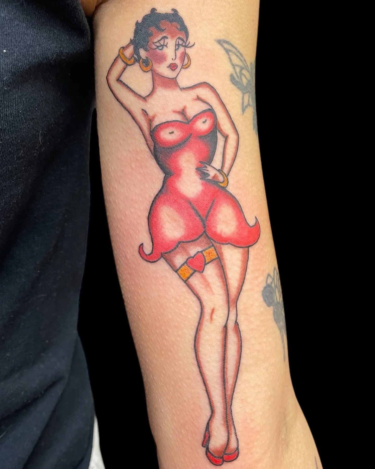 A bold, vintage-inspired pin-up tattoo with a devilish twist, featuring a confident woman in a red dress with horn-like details. The classic line work and vibrant color blocking give it a strong retro feel.
