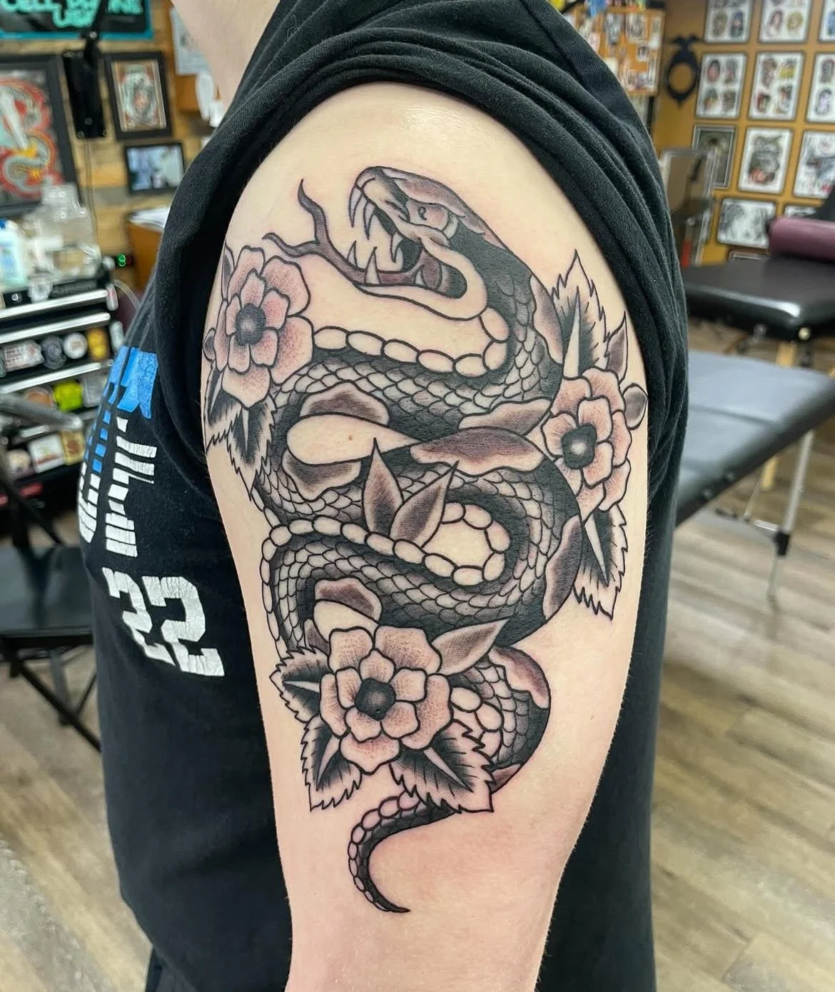 A coiled black and grey snake entwined with bold floral designs. The classic shading and composition highlight traditional tattoo aesthetics with strong movement and contrast.