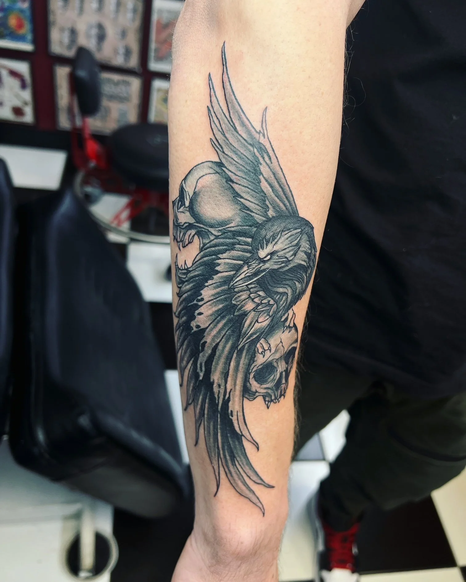 A black and grey piece featuring detailed skulls entwined with large, flowing wings. The fine shading and movement give it a dark yet dynamic, almost angelic energy.