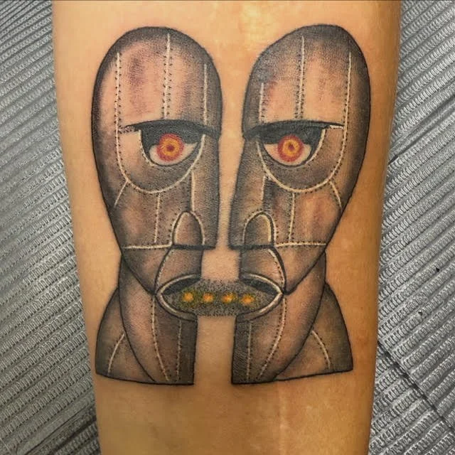 A detailed tattoo inspired by Pink Floyd’s The Division Bell album cover. The metallic tones, symmetry, and subtle shading recreate the surreal, thought-provoking essence of the original artwork.