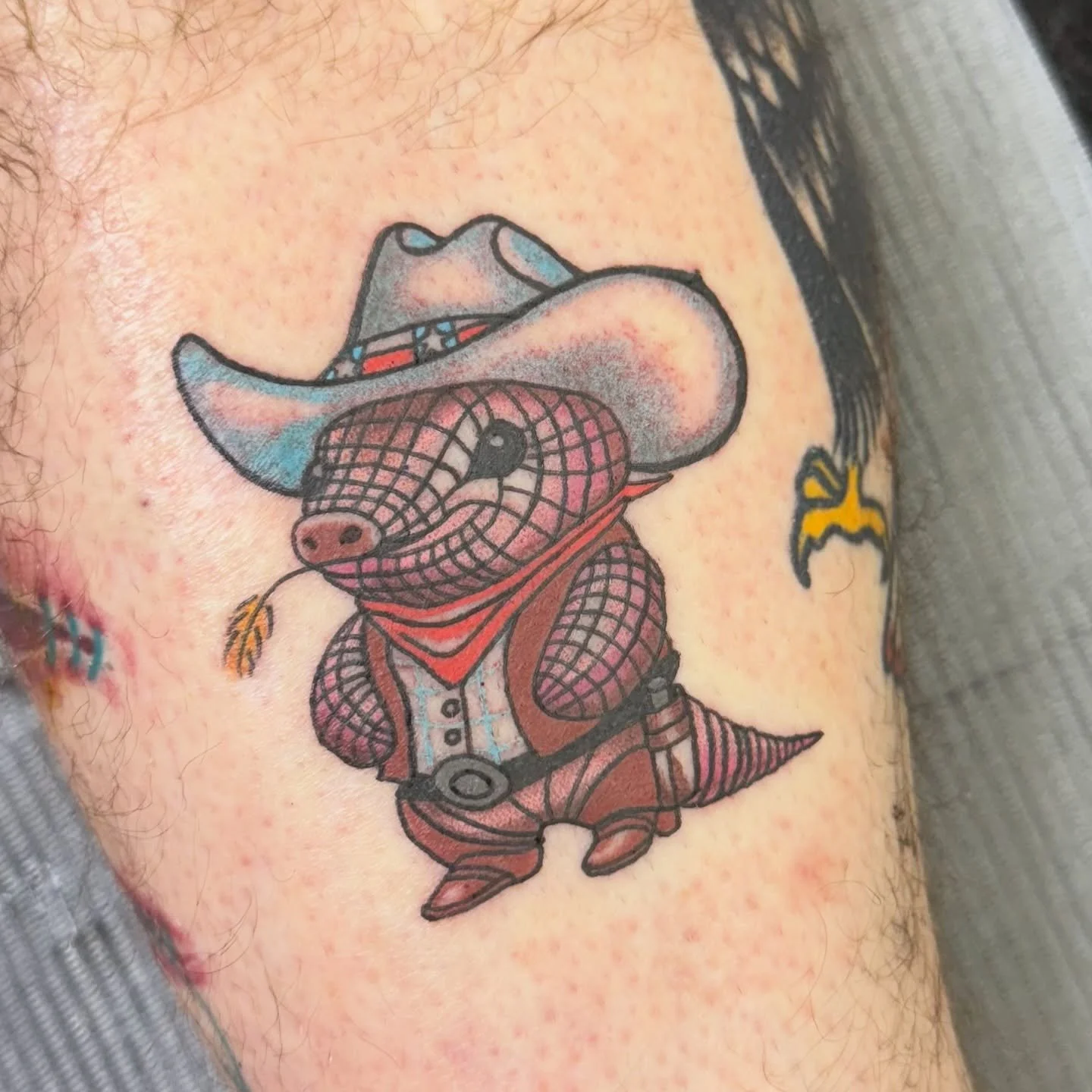 This playful design depicts a cowboy armadillo complete with a hat, vest, and bandana. The bright colors and cartoon styling make it a fun and lighthearted tattoo with a western twist.