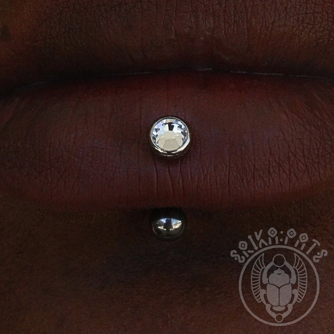 Close-up of a labret piercing with a clear gemstone on dark skin.