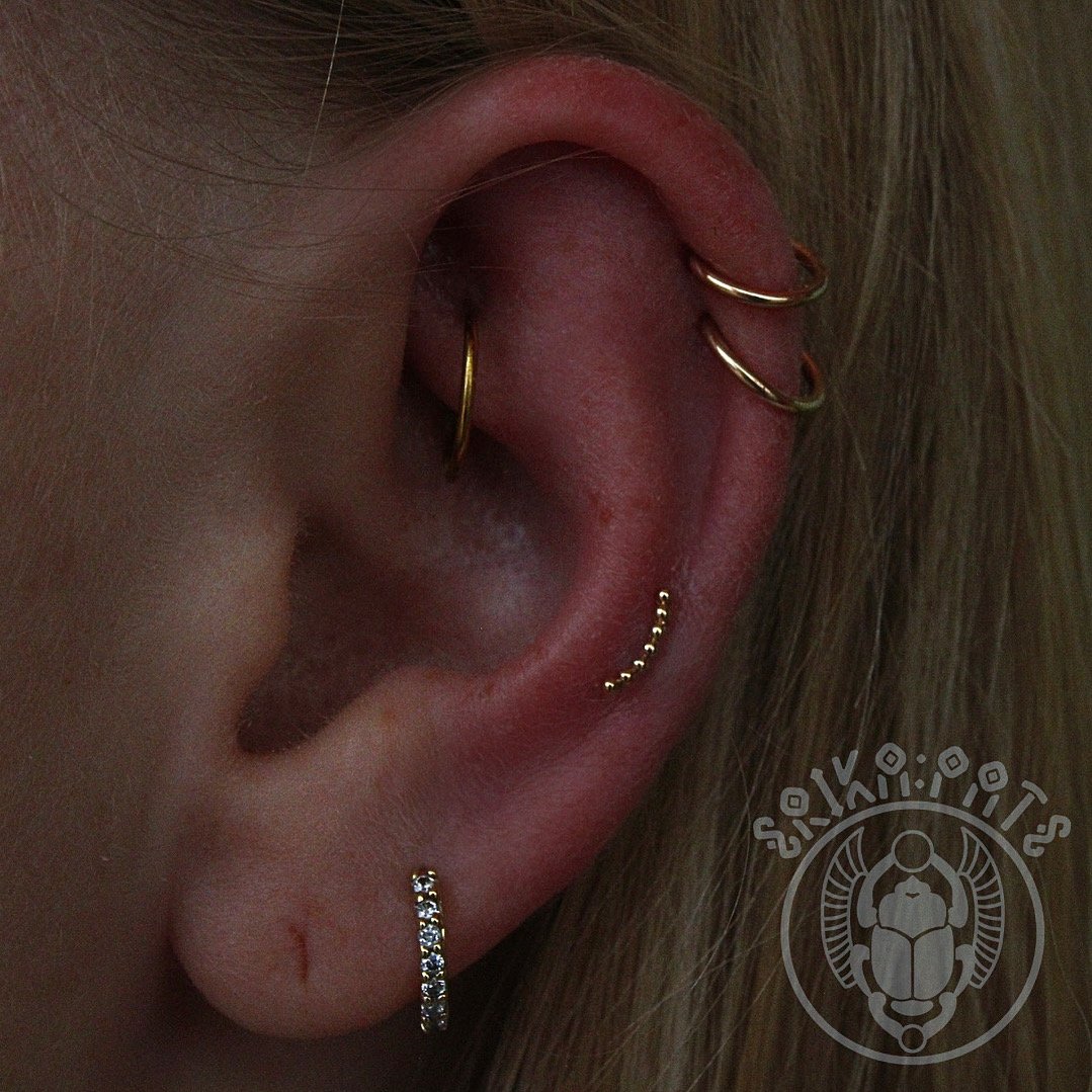 A beautifully balanced ear curation featuring multiple gold hoops and studs throughout the helix and lobe. The coordinated jewelry creates a cohesive and elevated look tailored to the wearer’s anatomy.
