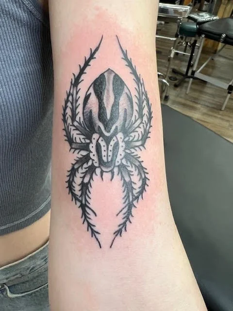 A striking black and grey spider design featuring symmetrical linework and fine detail. The bold contrast and clean composition make this piece both elegant and edgy.
