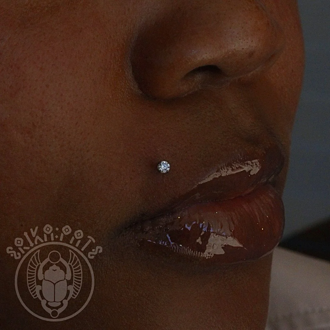 A Monroe piercing sits just above the upper lip, creating a subtle yet striking accent reminiscent of Marilyn Monroe’s iconic beauty mark. The flat-back labret stud offers both comfort and elegance.