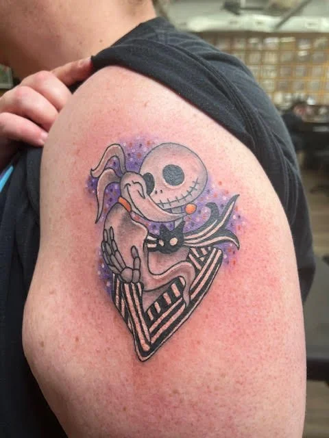 A whimsical tattoo of Jack Skellington holding Zero, surrounded by a glowing purple aura. The fine linework and bright color accents capture the playful, gothic charm of The Nightmare Before Christmas.