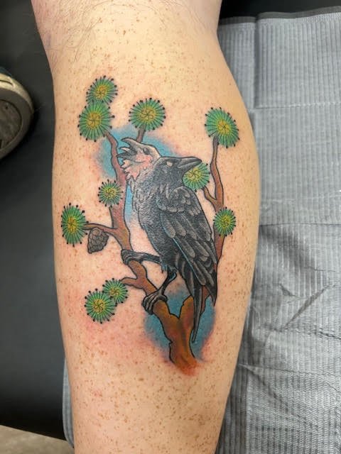 A bold, illustrative raven perched among stylized green blossoms with soft blue background shading. The color layering and crisp outlines give this design striking contrast and natural flow.