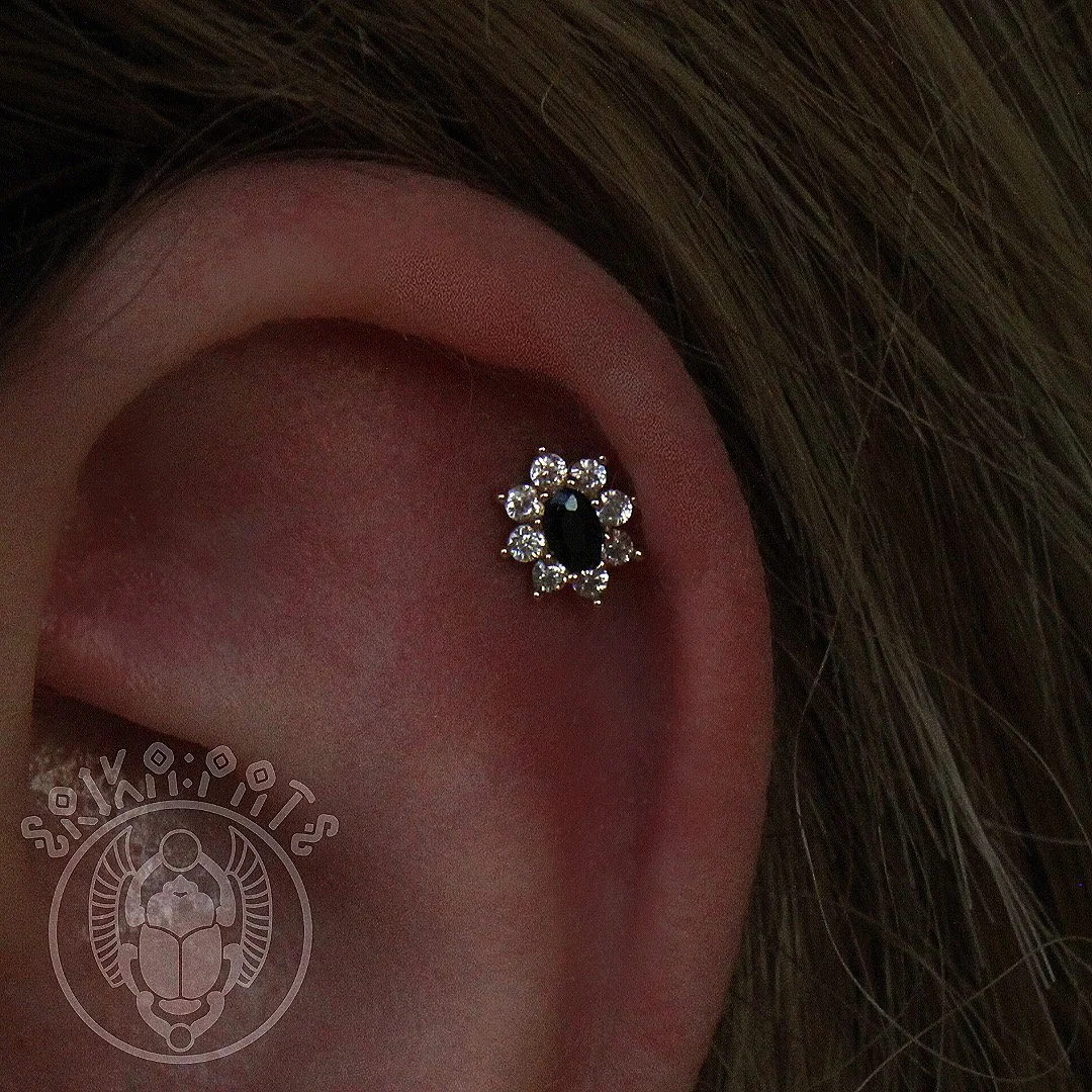 Close-up of a person's pierced ear with a decorative black and silver earring, with brown hair partially visible.