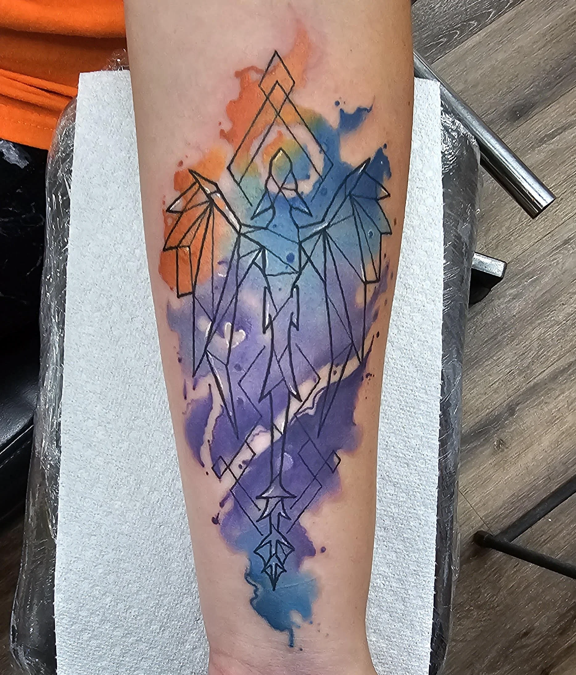 A sleek, geometric-styled phoenix rises upward through a wash of blue, purple, and orange watercolor tones. The clean linear design over soft blended color gives the piece a modern, symbolic, and ethereal look.