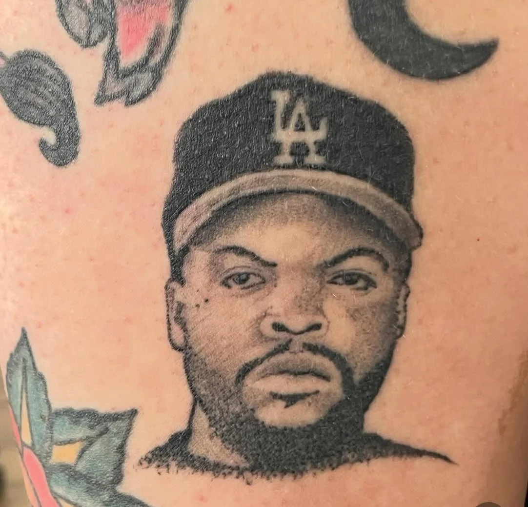 A detailed black and grey portrait of the iconic rapper Ice Cube, showcasing expert shading and crisp realism. The subtle texture and expression capture his unmistakable presence and attitude, paying tribute to hip-hop culture.