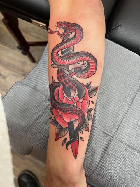 A coiled red and black snake wrapped around a dagger with bold floral accents. The strong composition and traditional styling convey motion, strength, and precision.