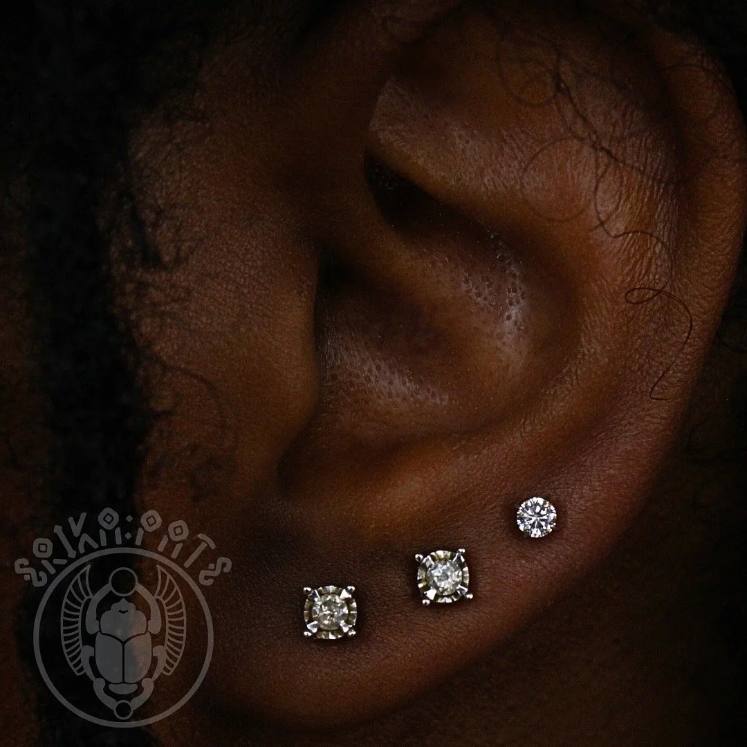 Close-up of a person's ear with three diamond earrings.