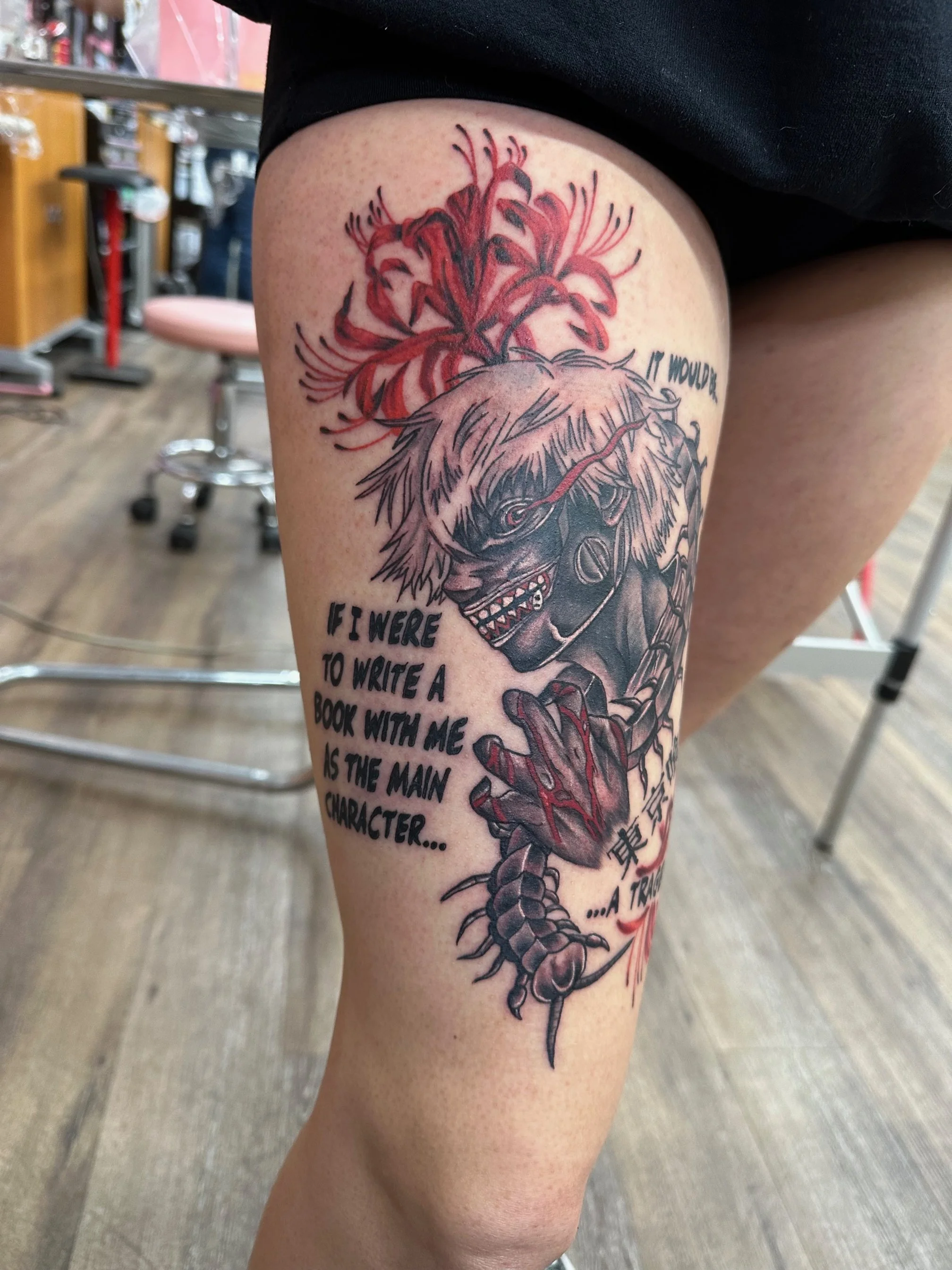An expressive anime-style tattoo in black and red ink, featuring intense contrast and dynamic linework. The floral background and text elements bring an emotional, story-driven edge to the design.