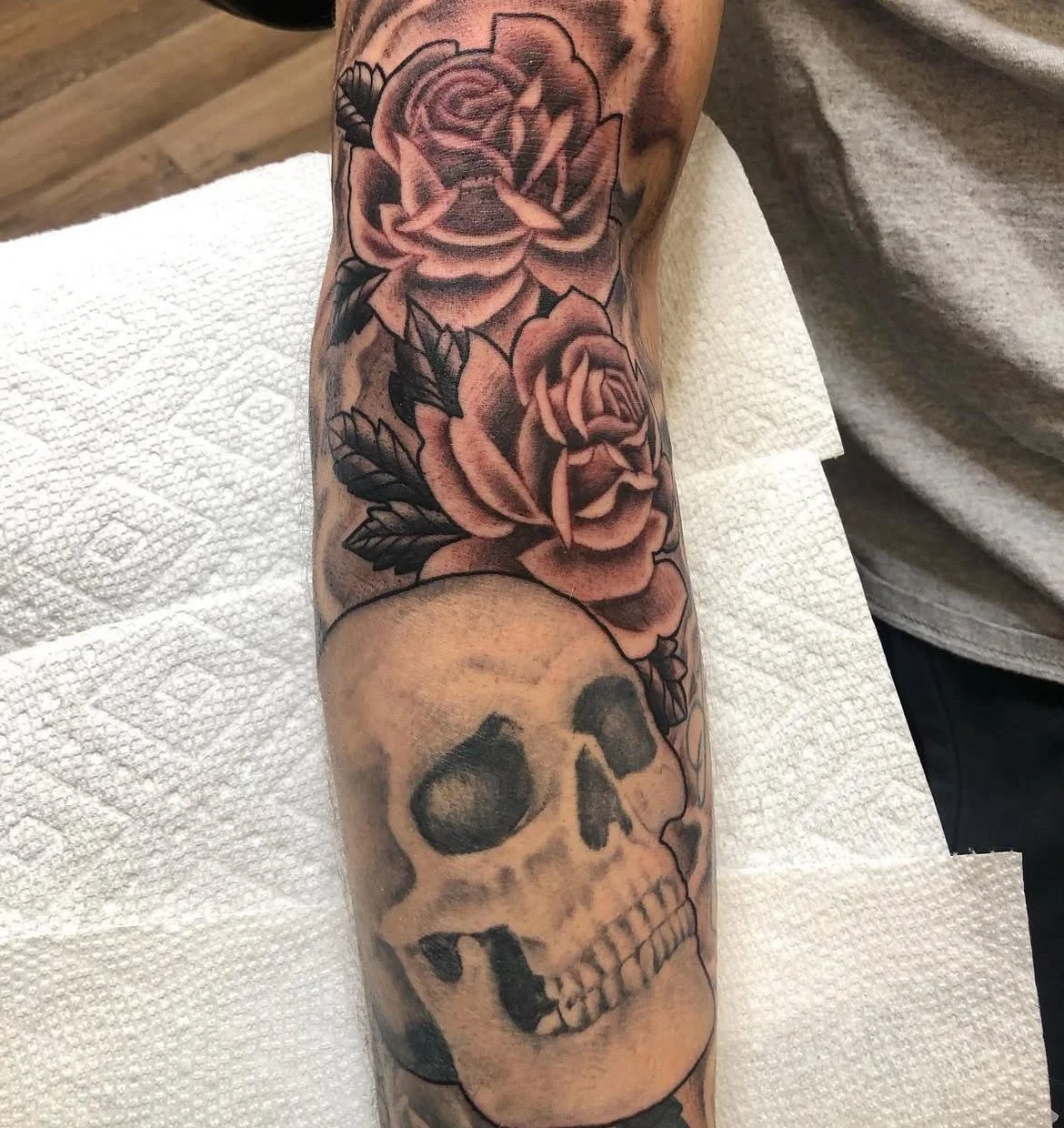A striking forearm design combining soft-shaded roses with a bold skull motif. The smooth gradient work creates an elegant contrast between beauty and mortality.