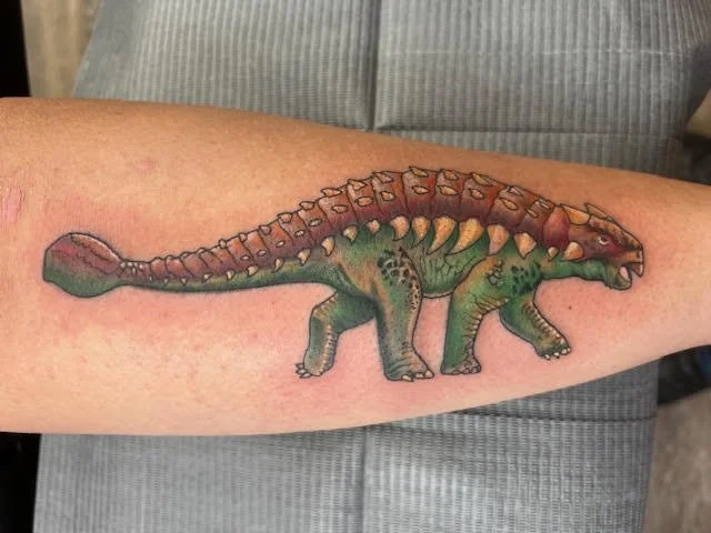 A colorful depiction of an ankylosaurus in realistic tones of green and brown. The attention to texture and shading gives the dinosaur a lifelike, dynamic quality.