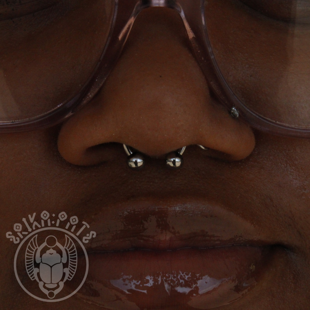 A septum piercing placed through the soft tissue between the nostrils, showcasing a sleek circular barbell. Its symmetry and versatility make it a bold yet classic facial statement.
