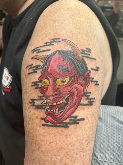 A traditional Japanese oni mask in striking reds and yellows, surrounded by stylized black smoke. The bold lines and dramatic color palette capture the energy and menace of classic Japanese folklore.