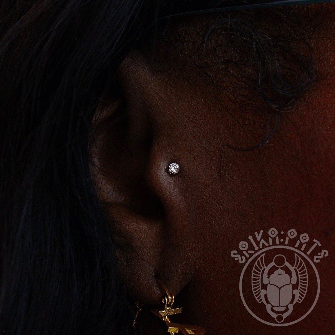 Close-up of a person's face showing their ear, with a nose piercing and a gold earring, and part of their curly hair.