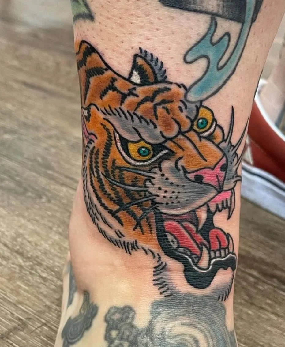 A bold traditional tiger head tattoo featuring saturated oranges and greens. Strong outlines and expressive detail give it a classic old-school feel.