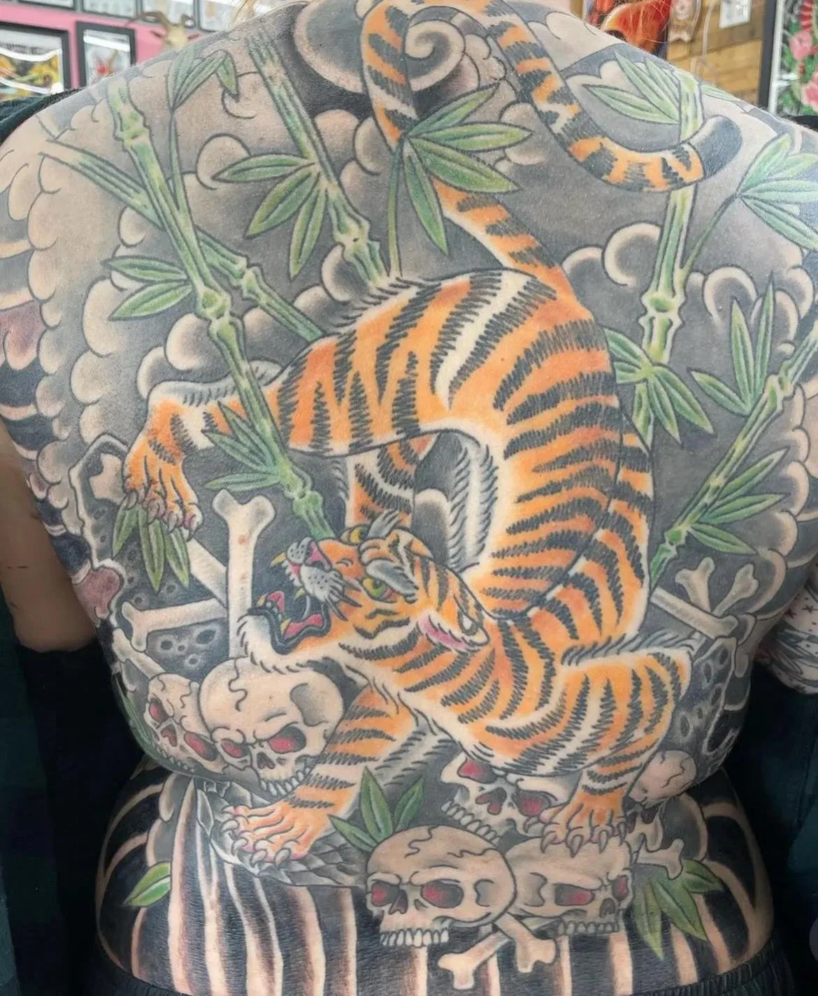 A large-scale Japanese-inspired backpiece featuring a fierce tiger surrounded by bamboo, skulls, and swirling clouds. The bold composition and traditional color palette showcase balance, power, and movement.
