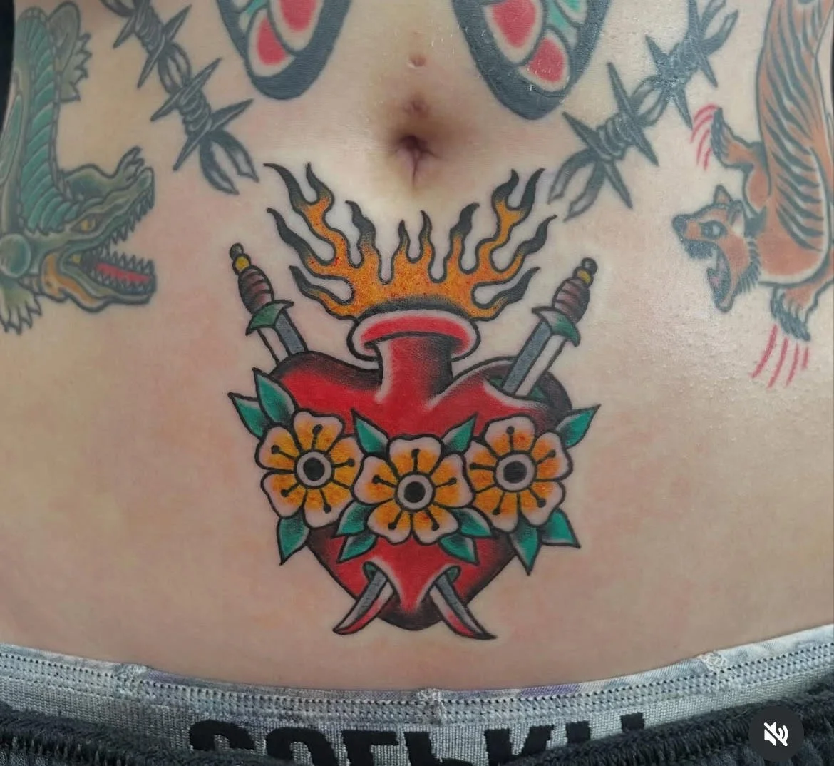 A vibrant neo-traditional Sacred Heart design with floral accents and fiery detailing. The bold reds and yellows create a dynamic focal point that symbolizes devotion and resilience.