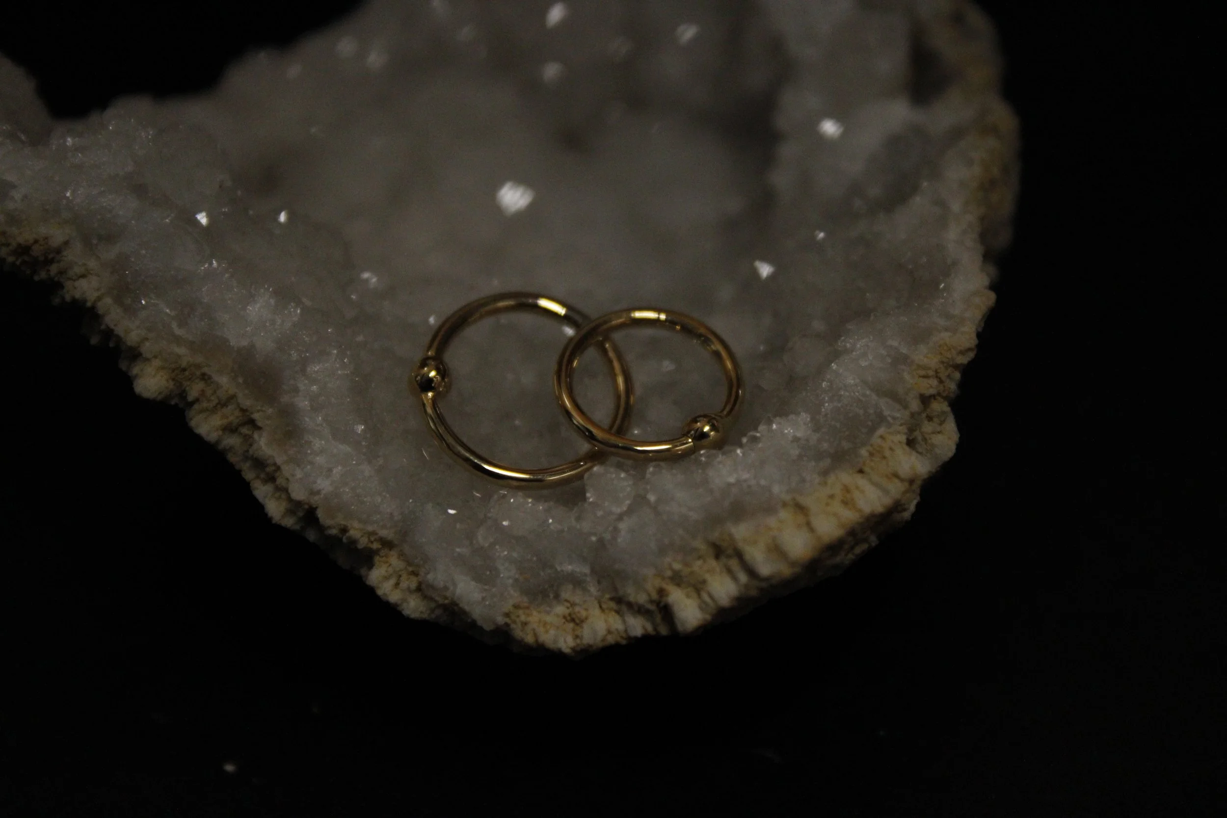 A pair of gold hoop earrings resting on a textured, crystalline rock with dark background.