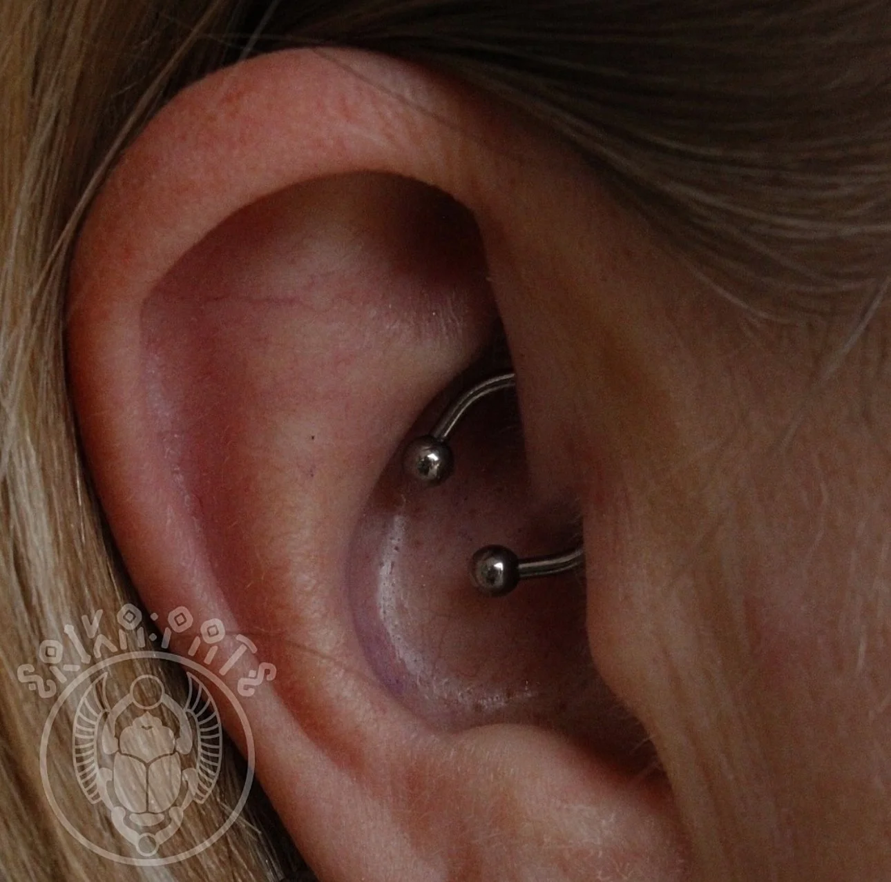 Close-up of a person's ear with a double helix piercing with two metal studs.