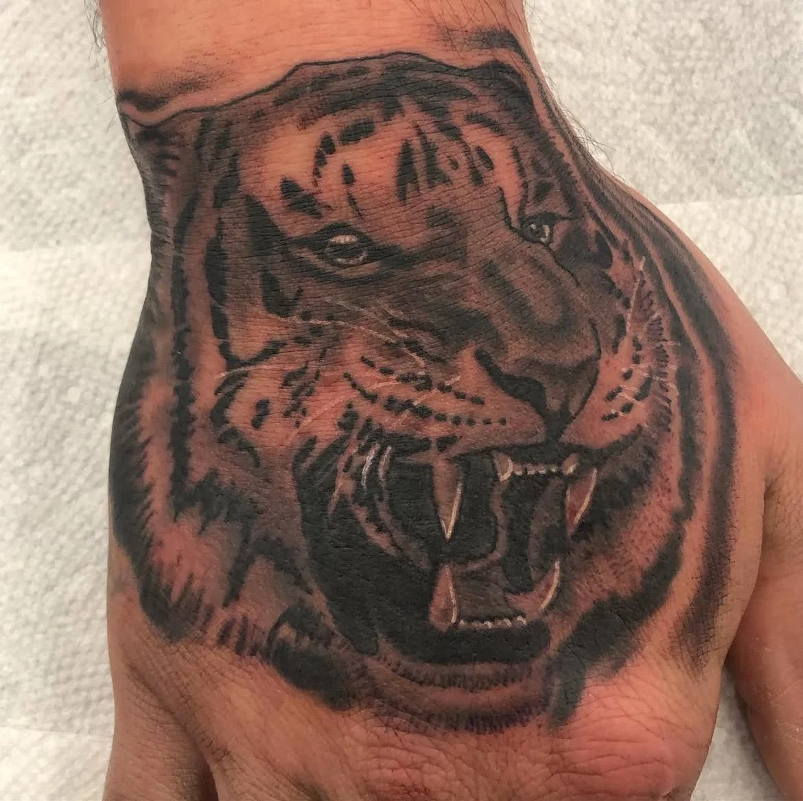 A roaring tiger head rendered in deep black and grey tones. The fine detailing and placement give this piece fierce energy and realism.