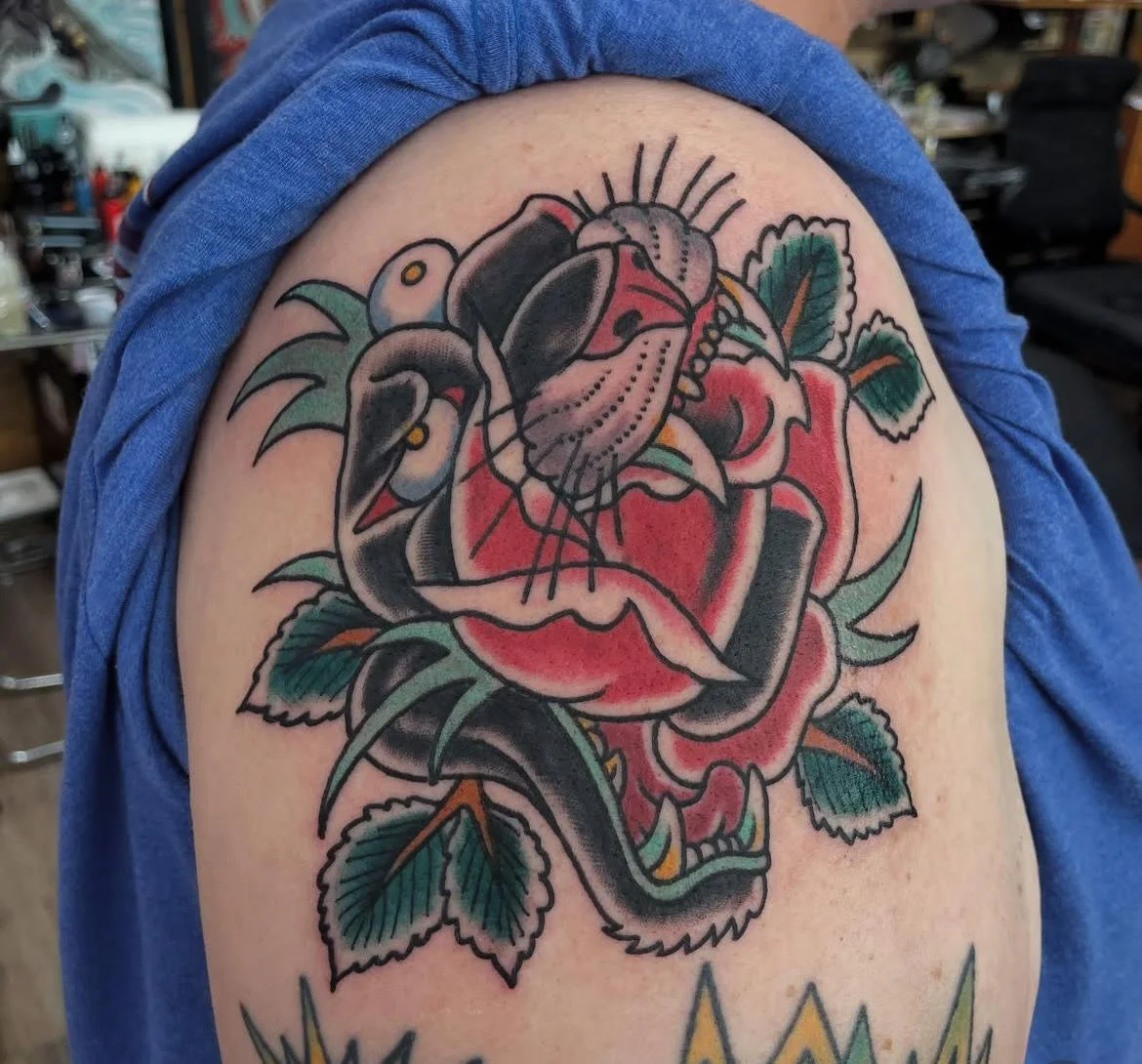 A coiled black panther intertwined with a red rose in true American traditional fashion. The bold lines, rich color palette, and timeless imagery embody classic tattoo heritage.