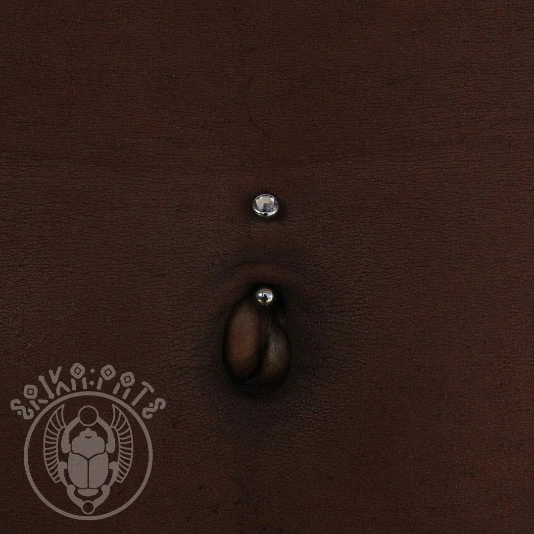 A classic navel piercing placed through the upper rim of the belly button, adorned with a curved barbell. This stylish and timeless choice complements the natural contour of the abdomen while healing beautifully with proper care.
