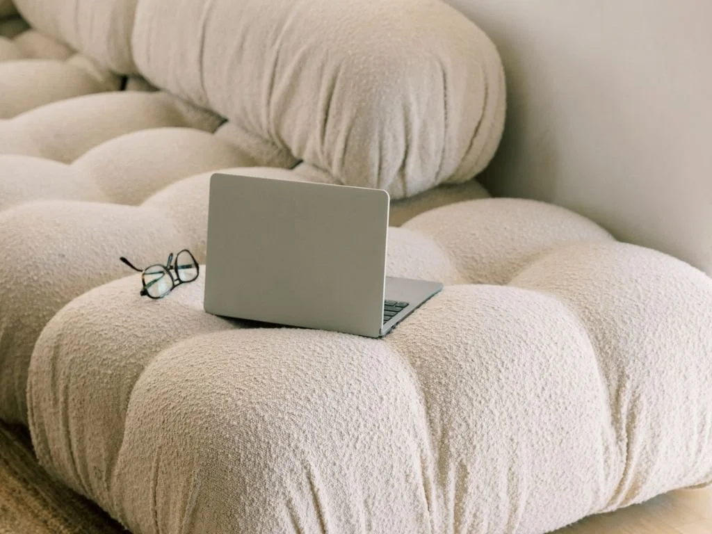 A tuxedo jacquard fabric sofa with plush cushions, a laptop, and eyeglasses resting on it.