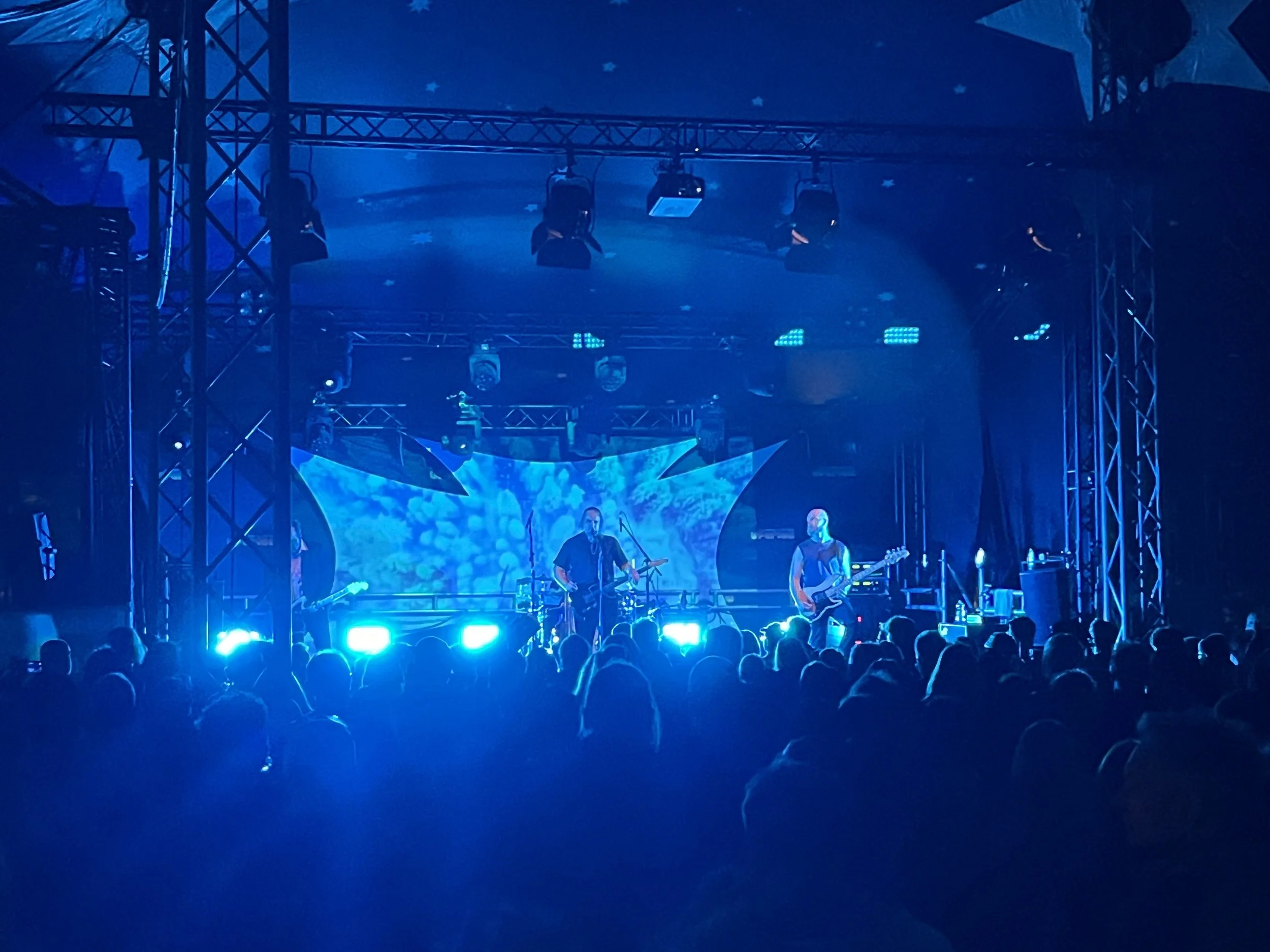 Auf einer Bühne spielen Musiker bei einer Konzertveranstaltung, umgeben von blauer Beleuchtung und modernem Bühnenaufbau.
Uferlos Festival Freising