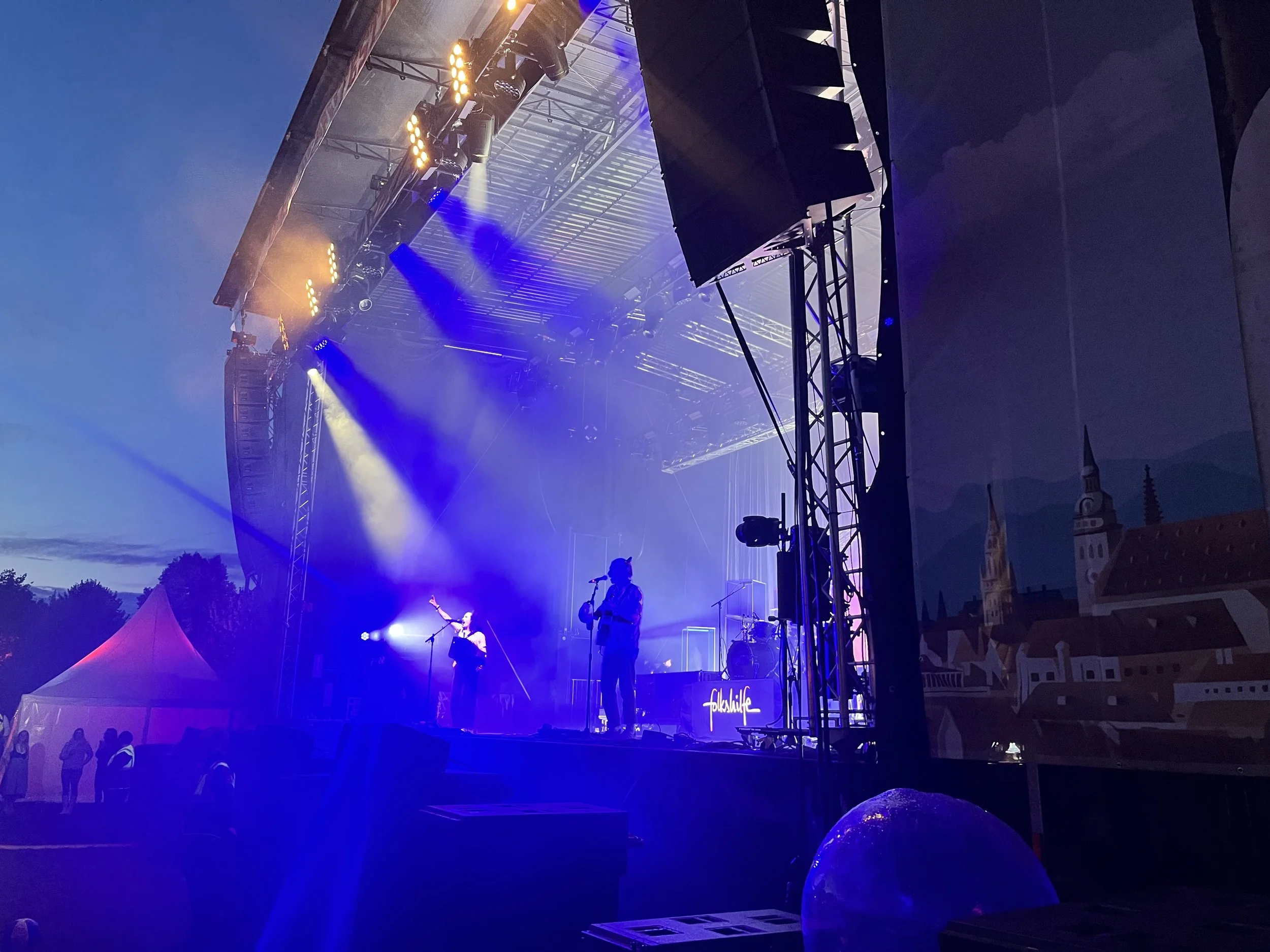 Bühne bei einem Abendkonzert mit blauen Licht, Musiker und Lautsprecher. Brass Wiesn Festival 2025