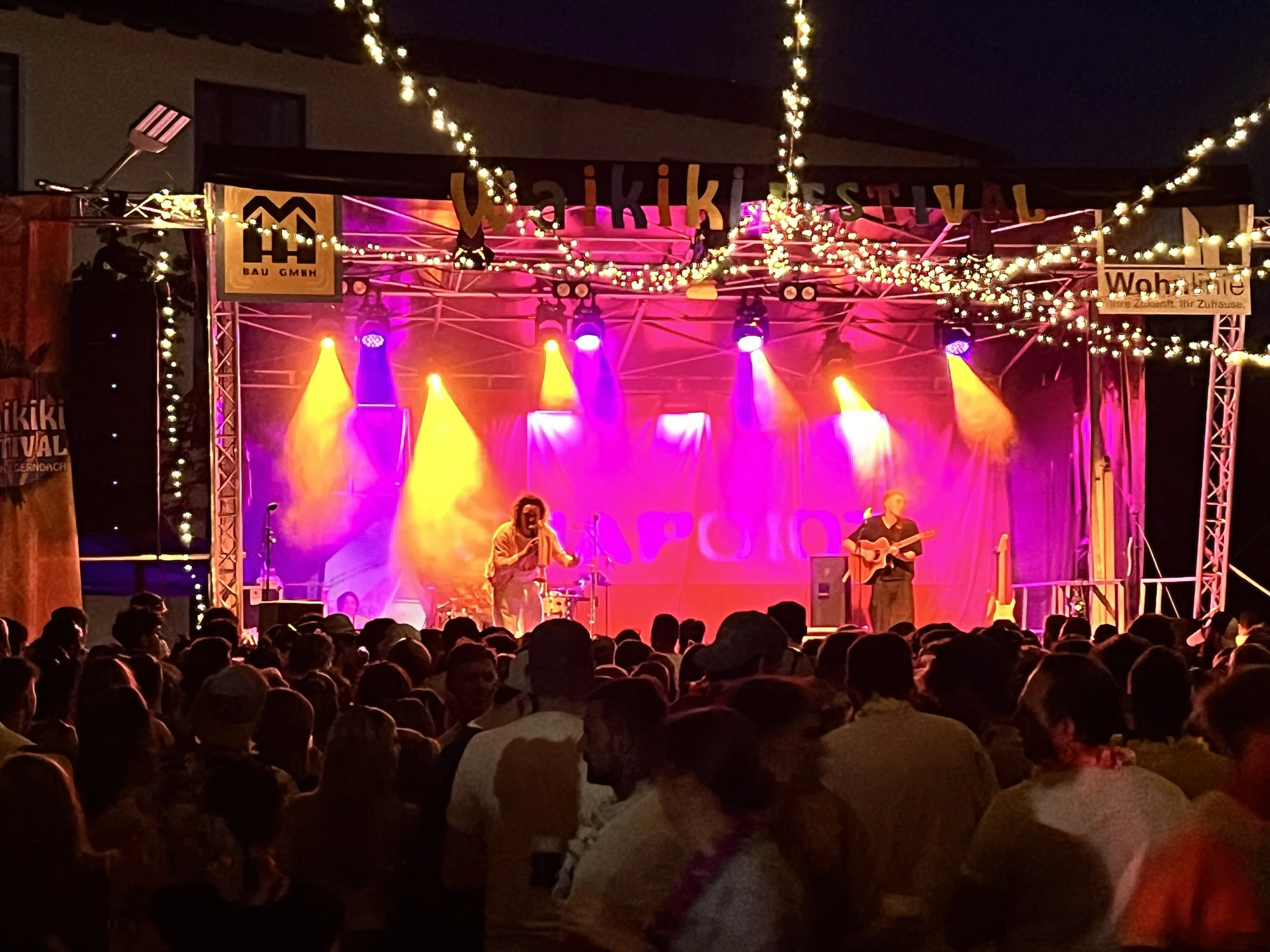Bühne bei einem Musikfestival abends, mit bunten Lichtern und einer Menschenmenge im Vordergrund. Waikiki Festival 2026 Staudach