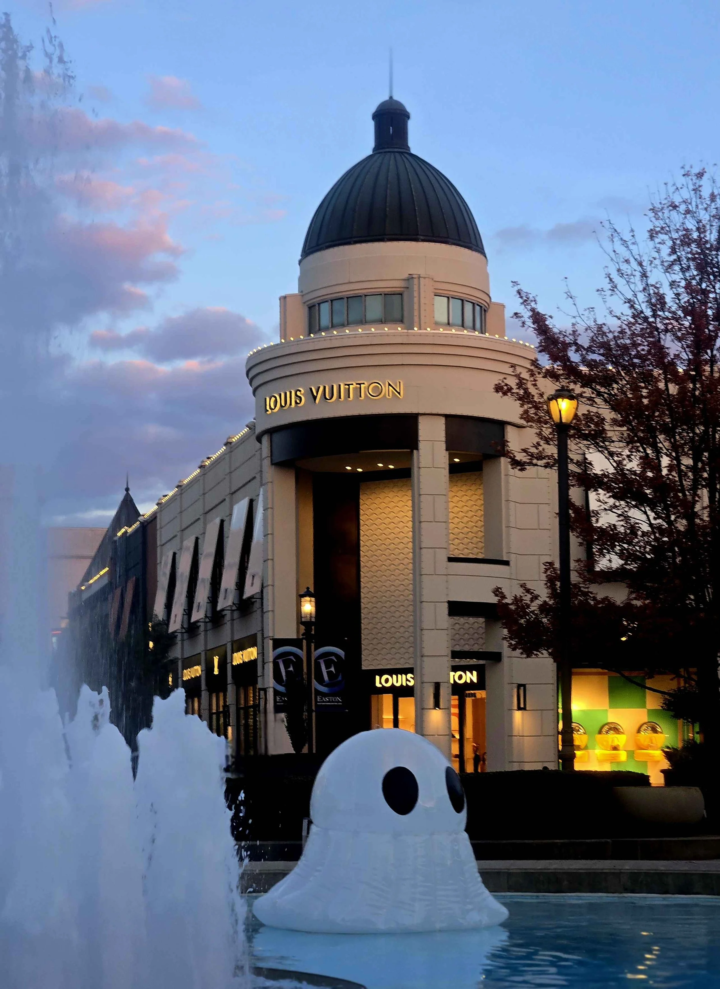 Louis Vuitton store in an outdoor shopping area at sunset with a large inflatable ghost figure in a fountain