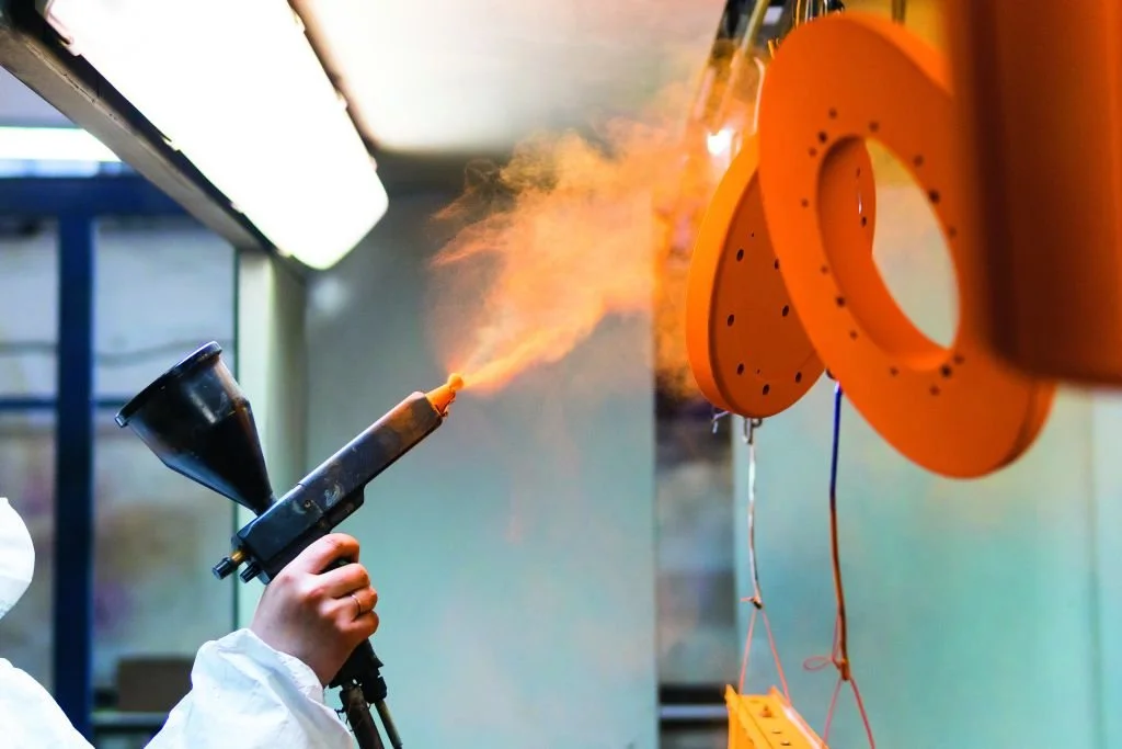 Person wearing protective suit using a blowtorch to melt or cut foam toy donuts hanging on a wall.