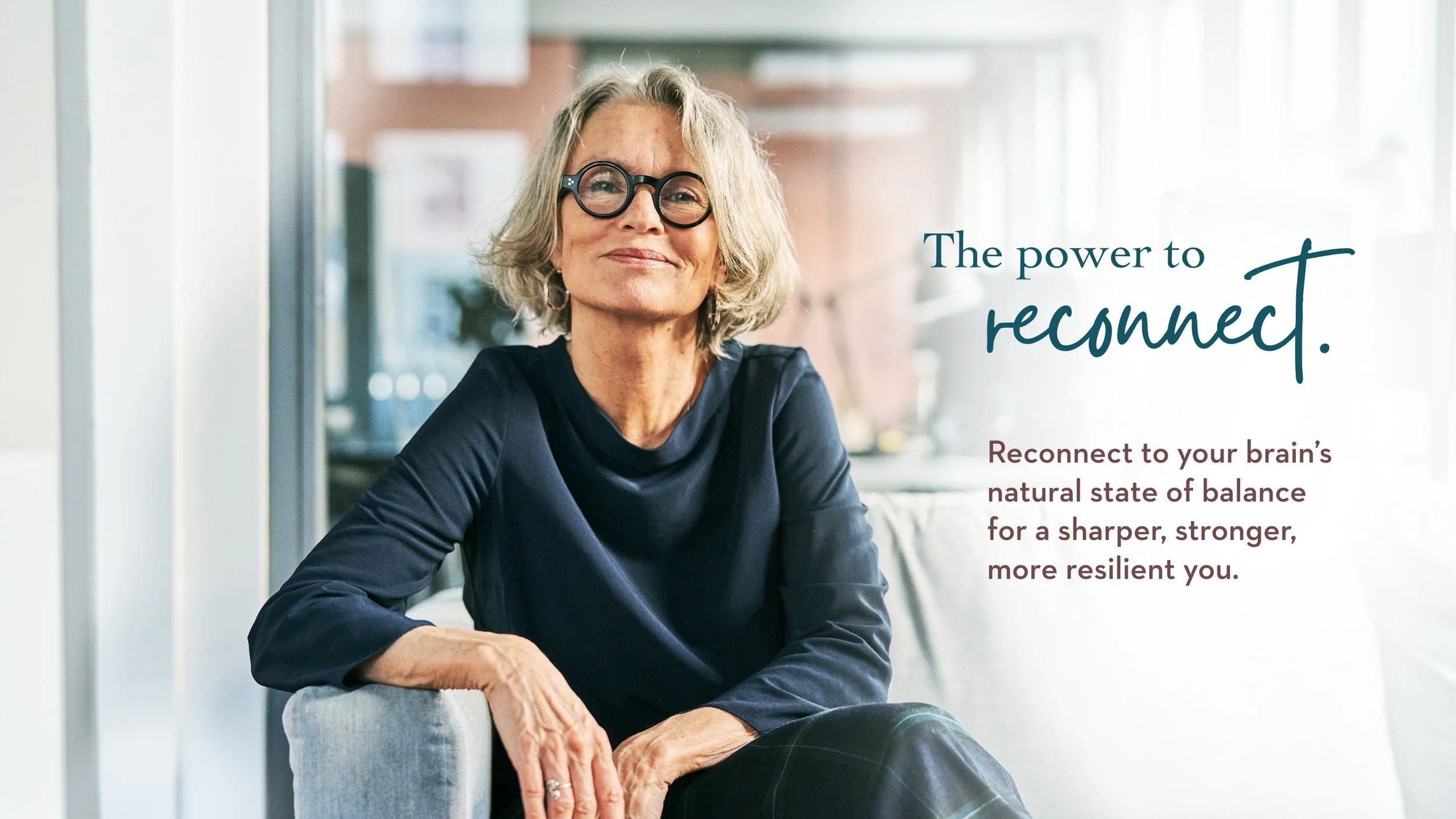 A confident older woman with short gray hair and round glasses sits on a sofa, smiling softly. Beside her, text reads: “The power to reconnect. Reconnect to your brain’s natural state of balance for a sharper, stronger, more resilient you.”